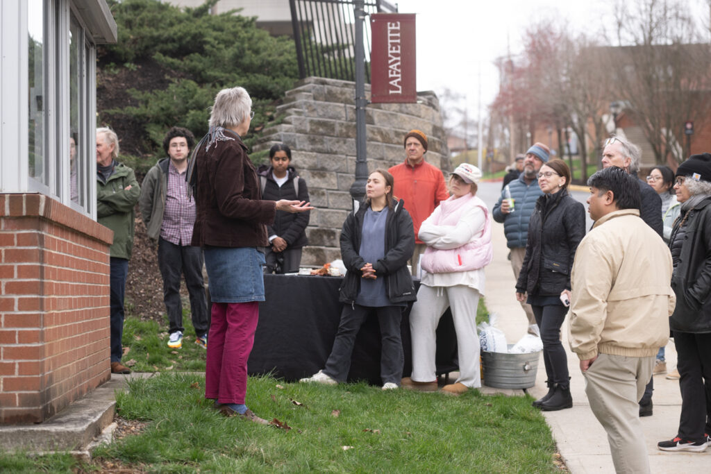 An artist on the left side of the frame speaks to a crowd gathered to see the artist artwork displayed in an old guard house on Lafayette College's campus. 
