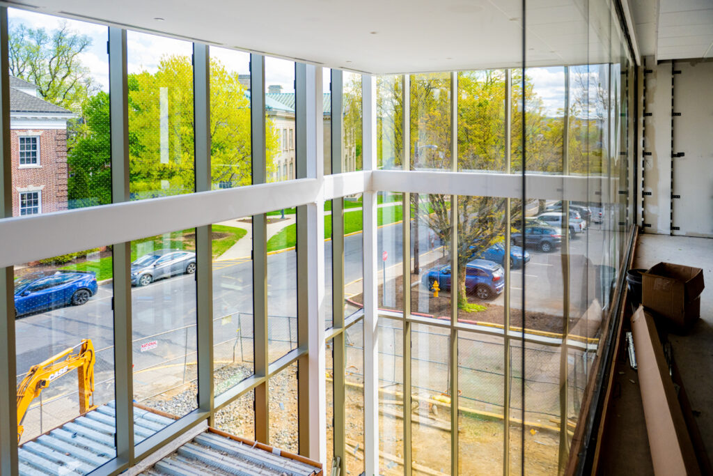 A photo taken inside a building with surrounding glass walls looking out to the street and parking lot.
