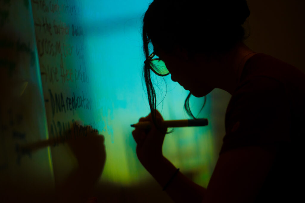 A close up silhouette of a person writing on a white board.
