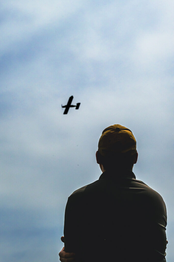 A student an remote controlled airplane are silouetted on a backdrop of clouds. 