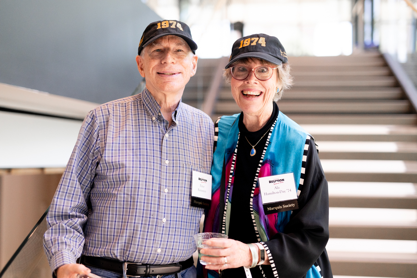 A man and woman pose for a photo on stairs in a modern academic building. They are wearing name tags