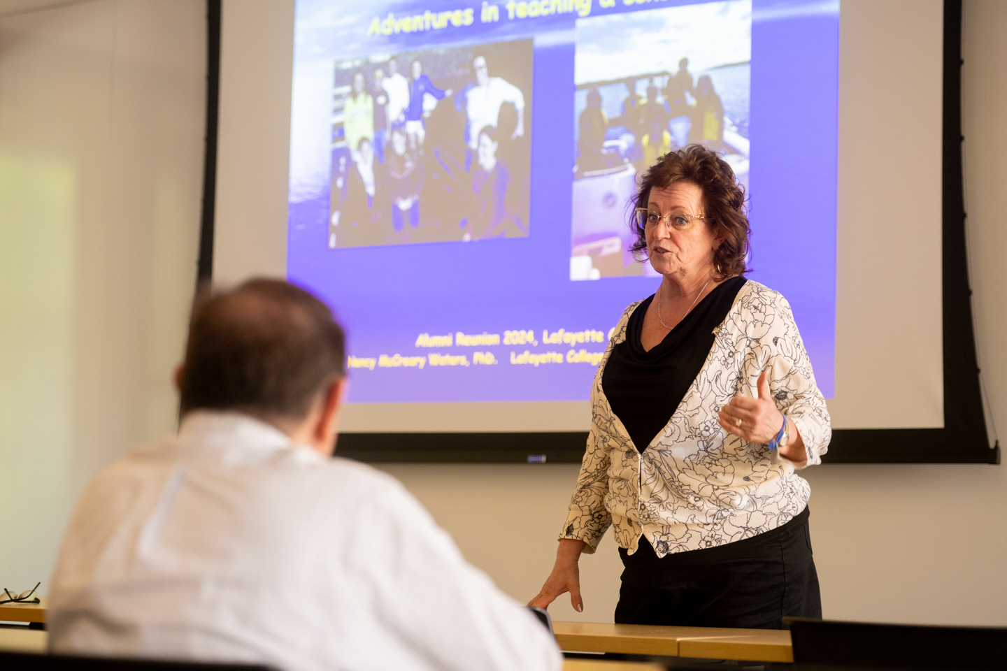 A woman professor speaks to a class of older college alumni. 
