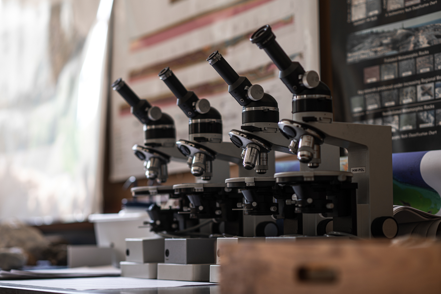 an array of microscopes are lined up next to each other in front of posters that illustrate different geological teaching aids. 