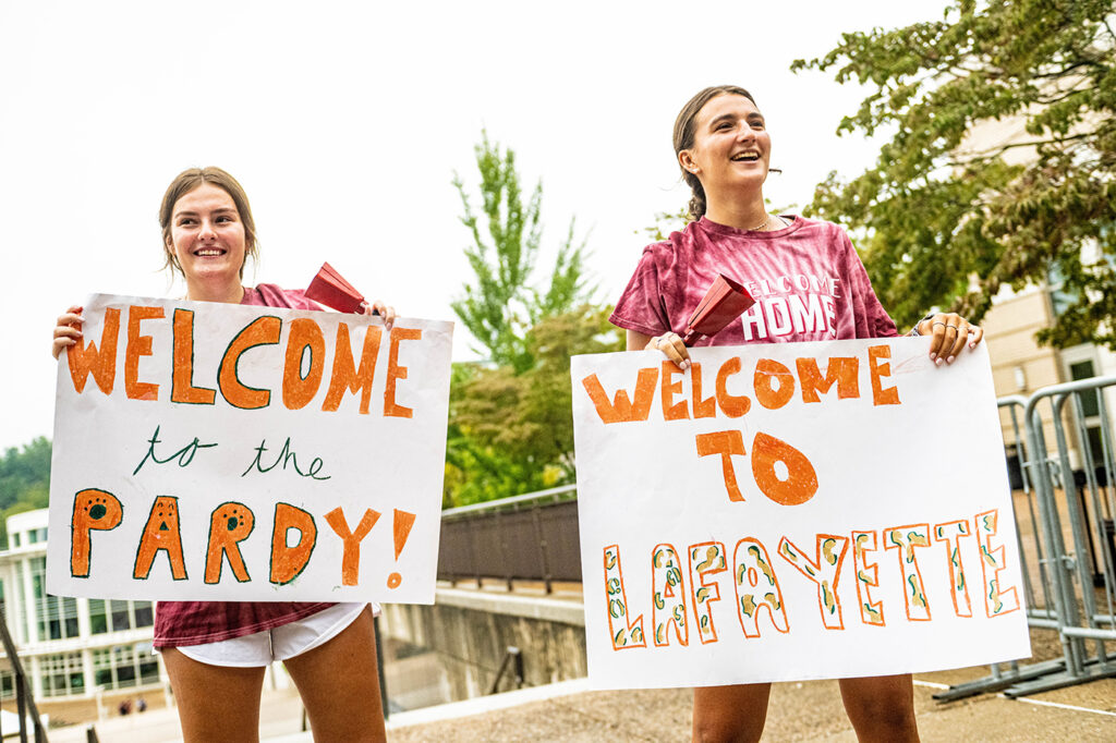 Two students hold up welcome signs reading Welcome to the Pardy and Welcome to Lafayette to greet other students during move in