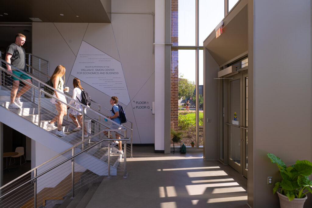 Side view of students walking down stairs towards the exit of the Simon Center for Economics and Business.