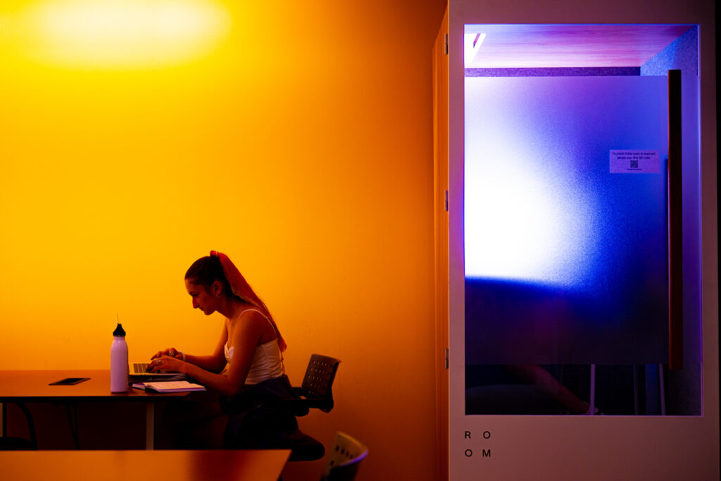 Side view of a person sitting at a table studying with a quiet booth illuminated next to them.