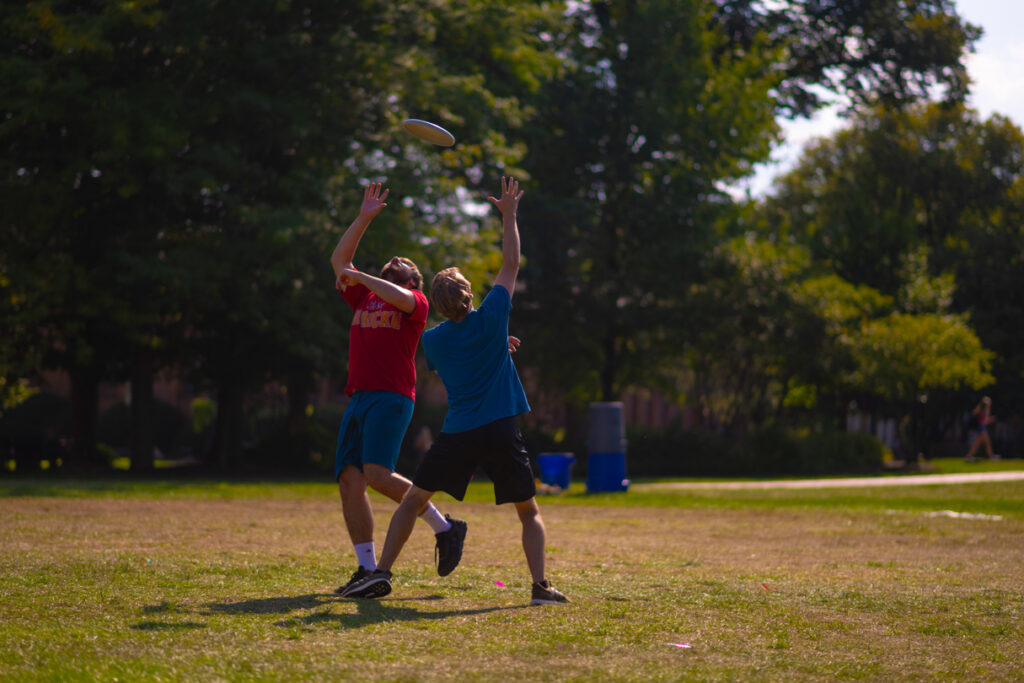 Two people reach up to catch a flying frisbee. 