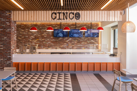 The interior of Cinco is shown with tile floor, back counter area with red lights, blue menu boards and the word Cinco.