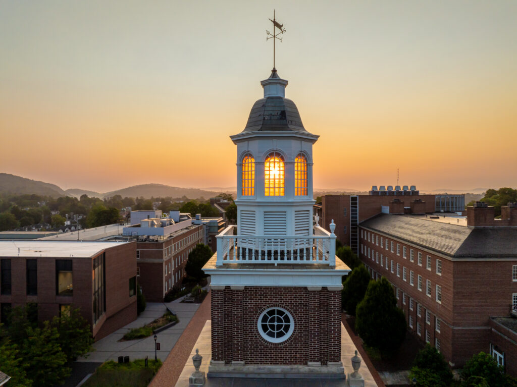 The sun shines through windows on top of a building cupola at sunrise.