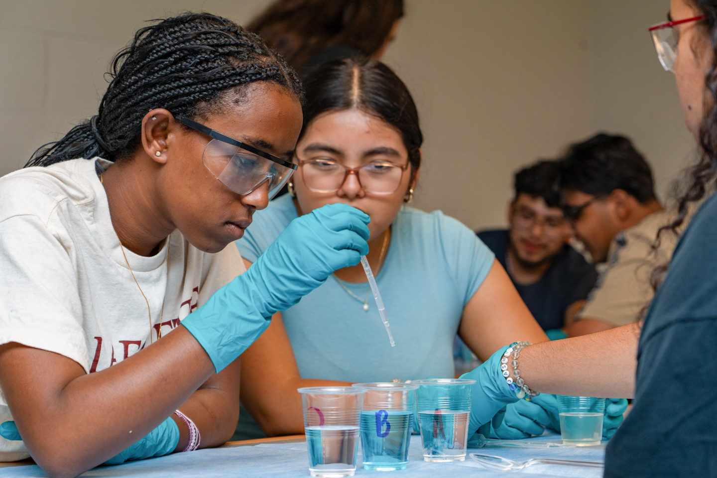 two female students on the left side of the frame, use a dropper to perform an experiment. 