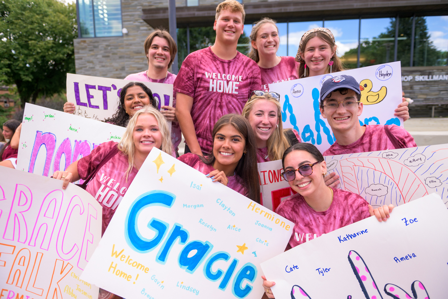 A group students pose on the steps of a building holding signs that identify what group they belong to. 