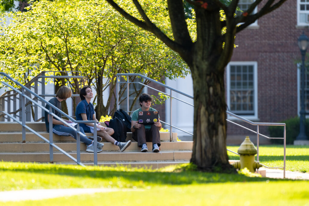 3 people sit on the steps of Hugel Science Center with their classwork.