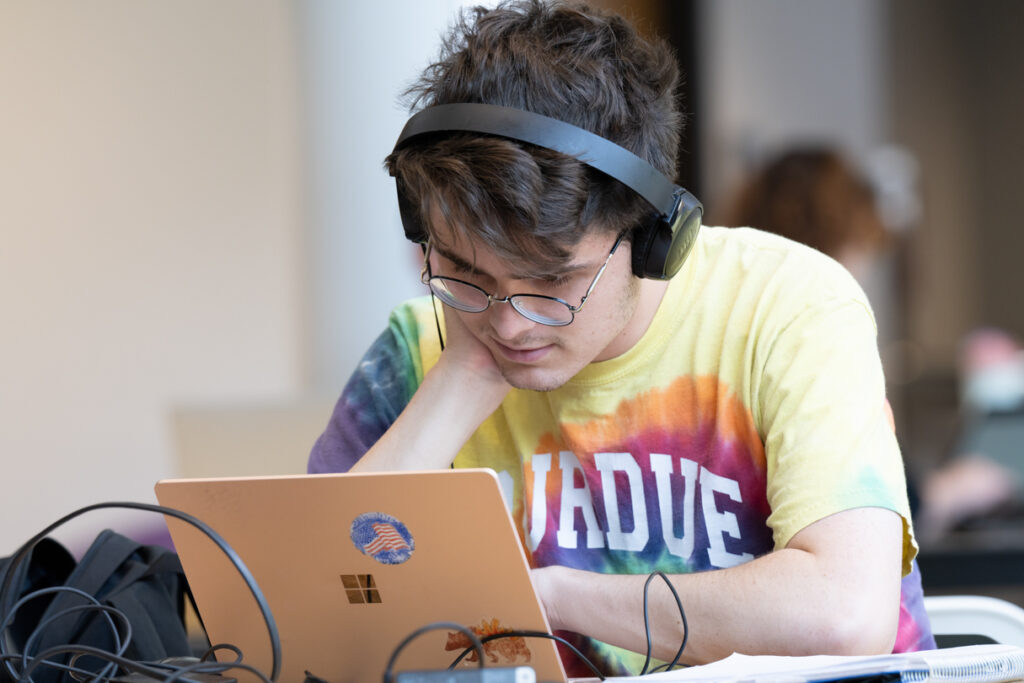 Close up of a student wearing headphones working on a laptop.