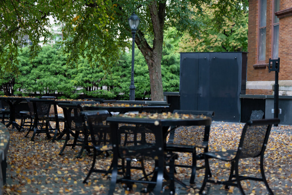 Leaves lay on outdoor tables and chairs next to an outdoor chalkboard.