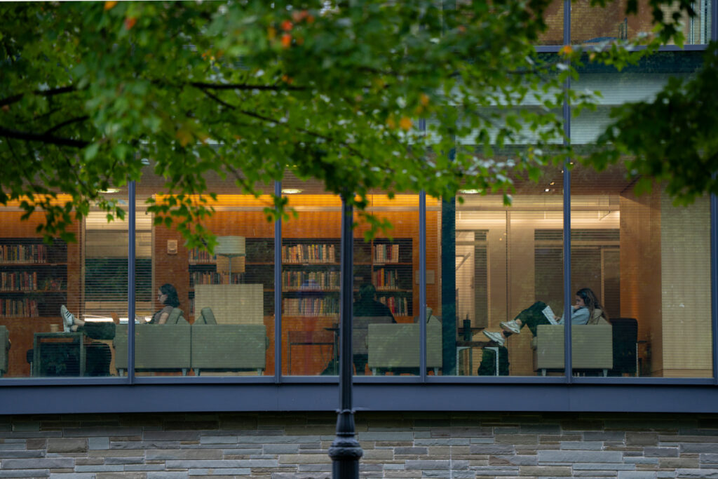 Looking through a far away window into people sitting on chairs in a library.