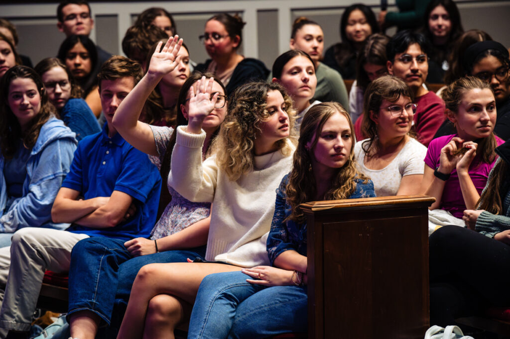 2 people raise their hands in a crowded room