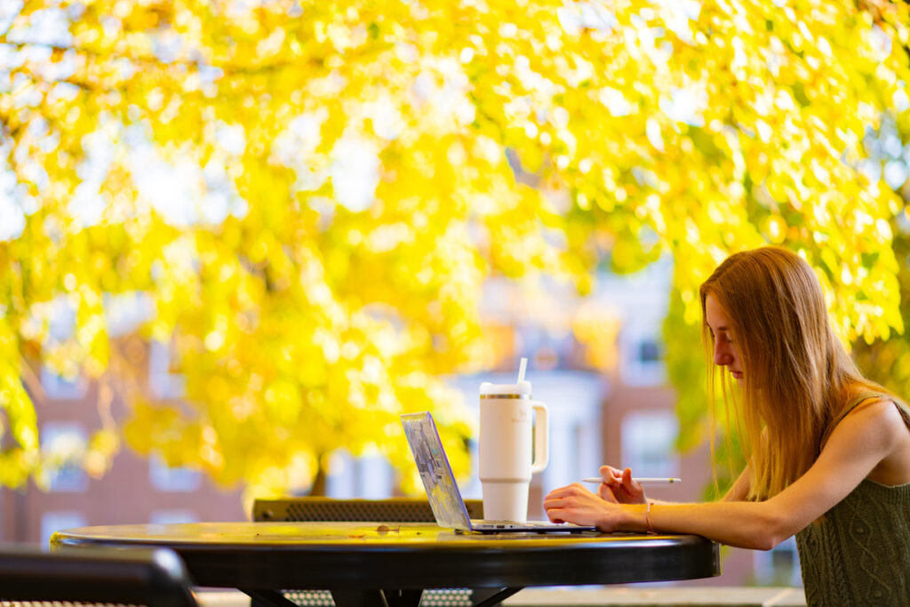 Side view of a person studying with fall foliage surrounding them.