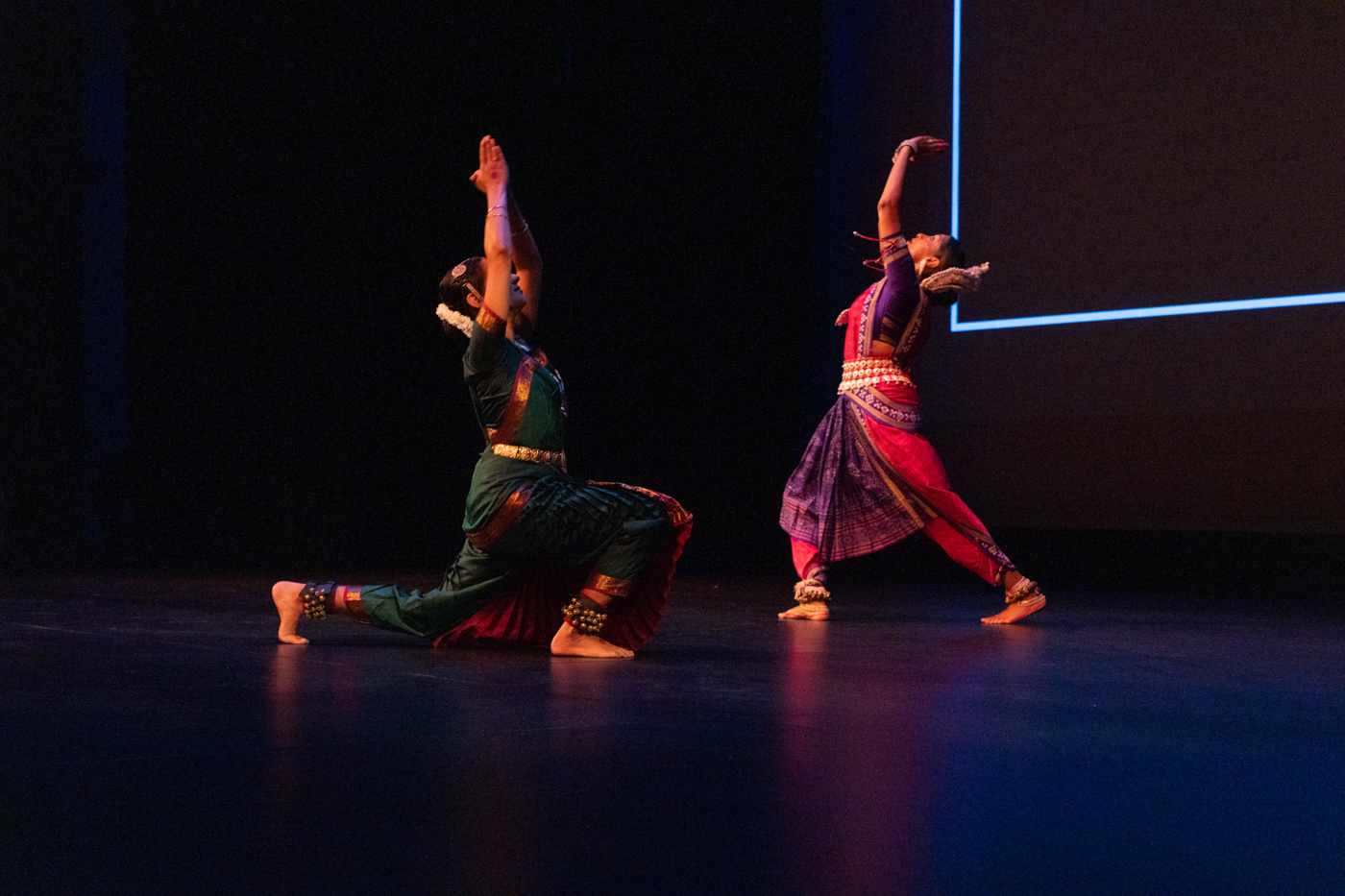 Two women are perform cultural dance on a dimly lit stage. 