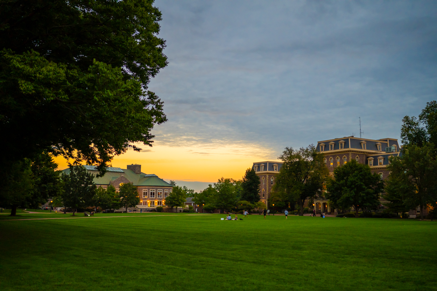 The sun sets on Lafayette College's Quad. In the center of the frame and in the distance a small group of students is gathered on a blanket. 