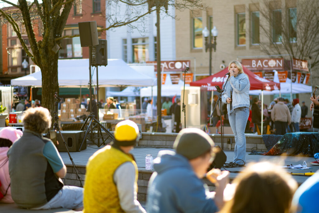 A person singing on a small outdoor stage in front of a small group of people.