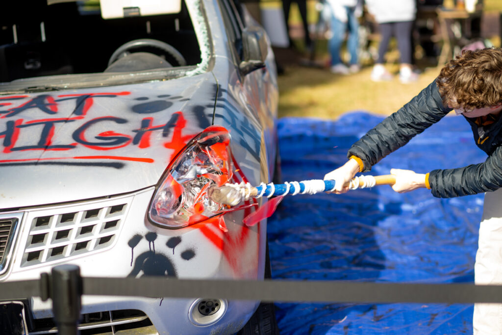 A sledgehammer hits the front light of a spray painted car.