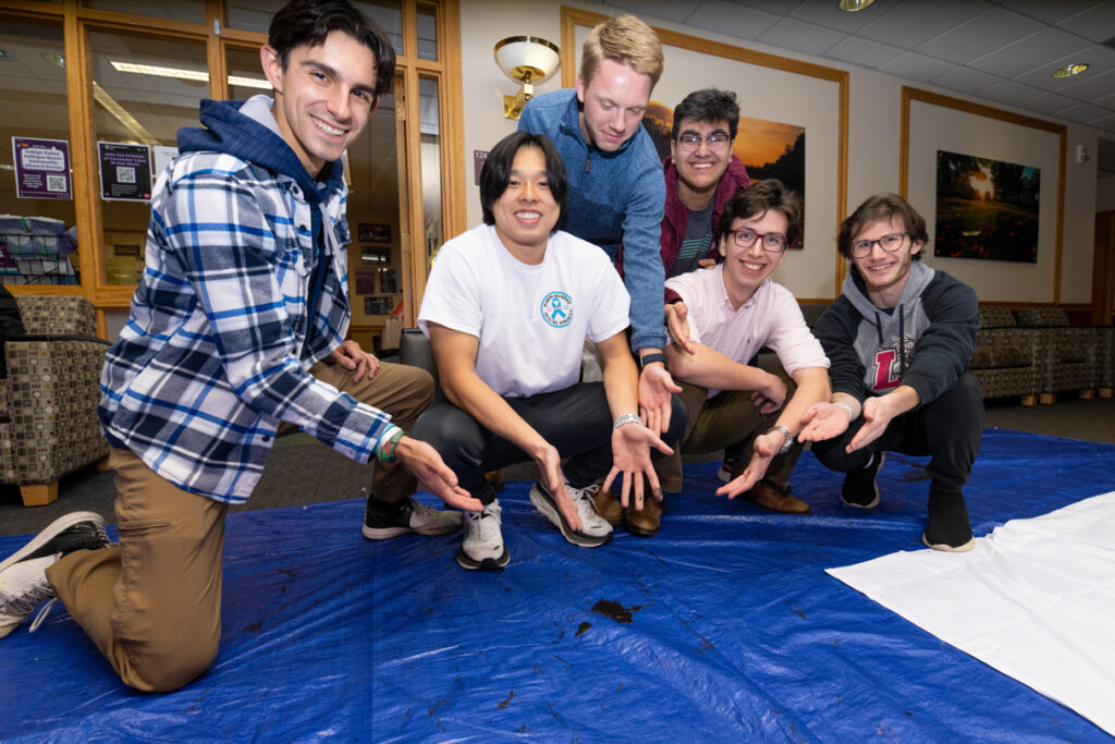 A group of people kneel around and point to a paint spill.