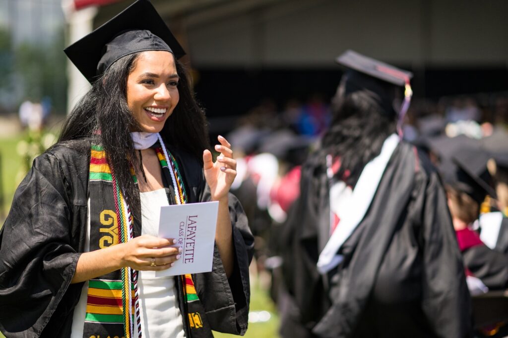 A Laf grad in cap and gown holds an envelope with a big smile on her face.