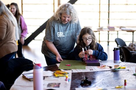 A Girl Scout leader helps her scout to craft a book in the library.