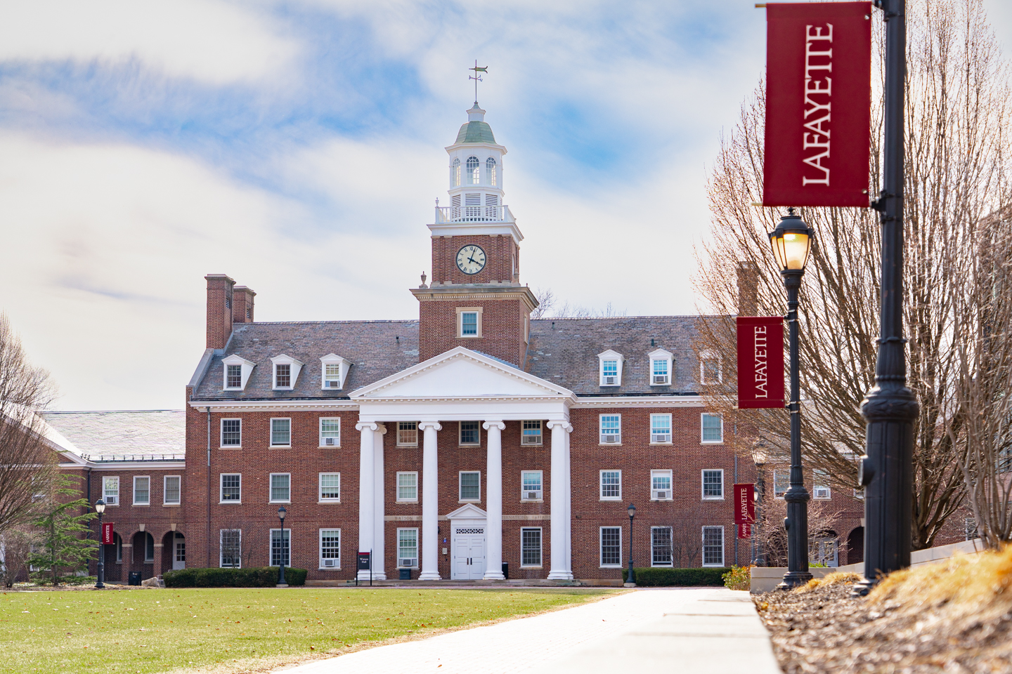 Residential building named Watson Hall at Lafayette College. The building has large columns in front of the doors and a big clock at the top. The building sits under a patchy blue sky.