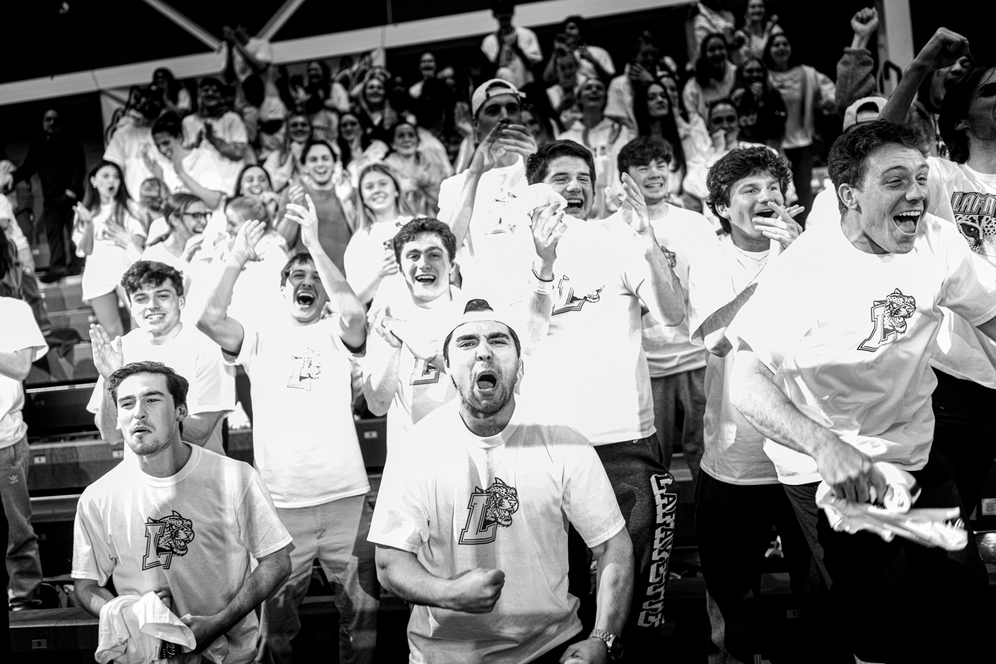 Fans at a basketball game cheering enthusiastically. They are all wearing white shirts with the Lafayette College logo