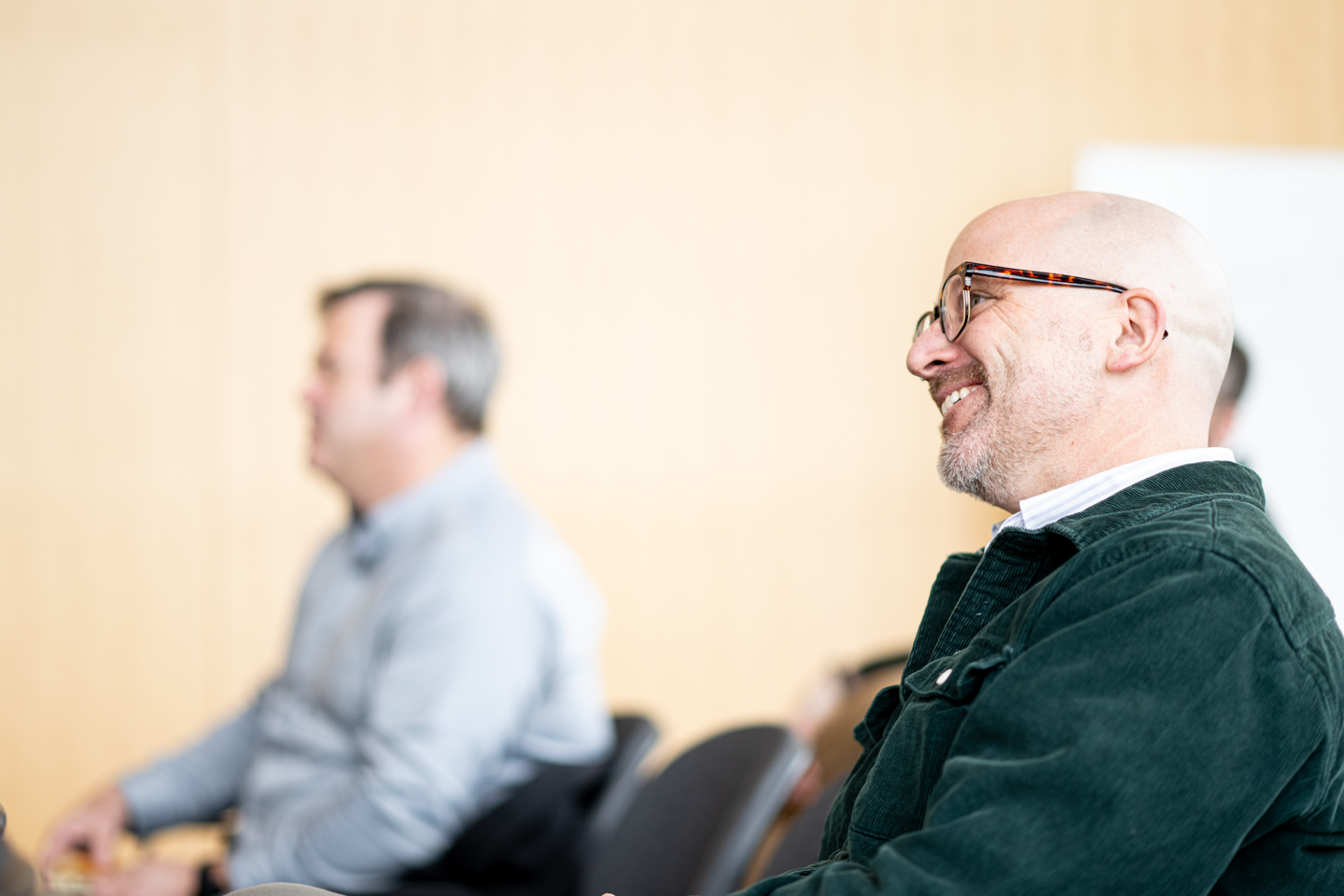 A faculty member smiling in the audience during the Faculty Features roundtable celebrating recent scholarly and creative works. 