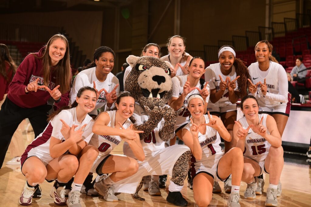 Women's basketball team is all smiles as they pose with the Leopard on the court.