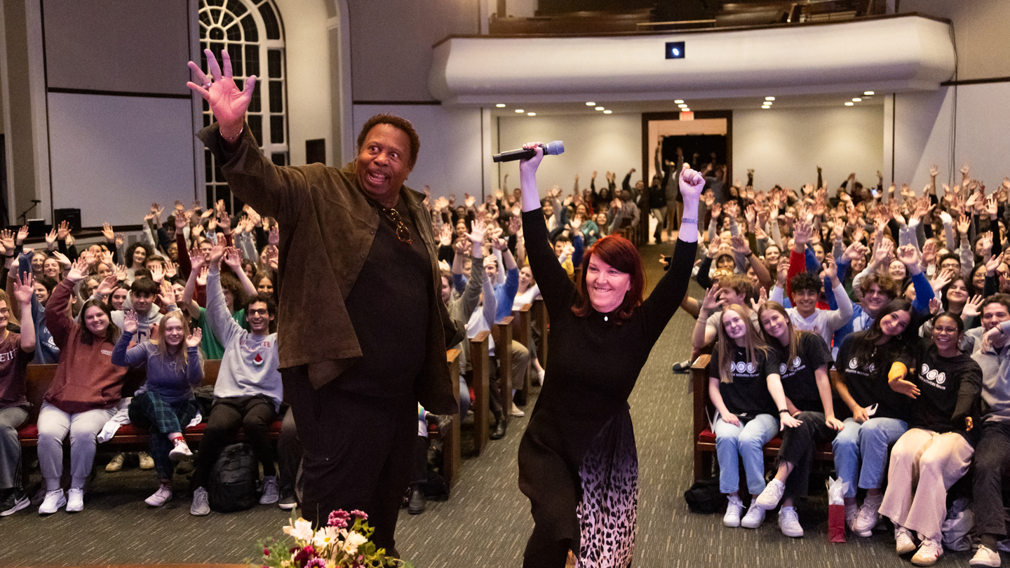 Kate Flannery and Leslie David Baker are cheering in front of a large crowd. The crowd is filled with students from Lafayette College.