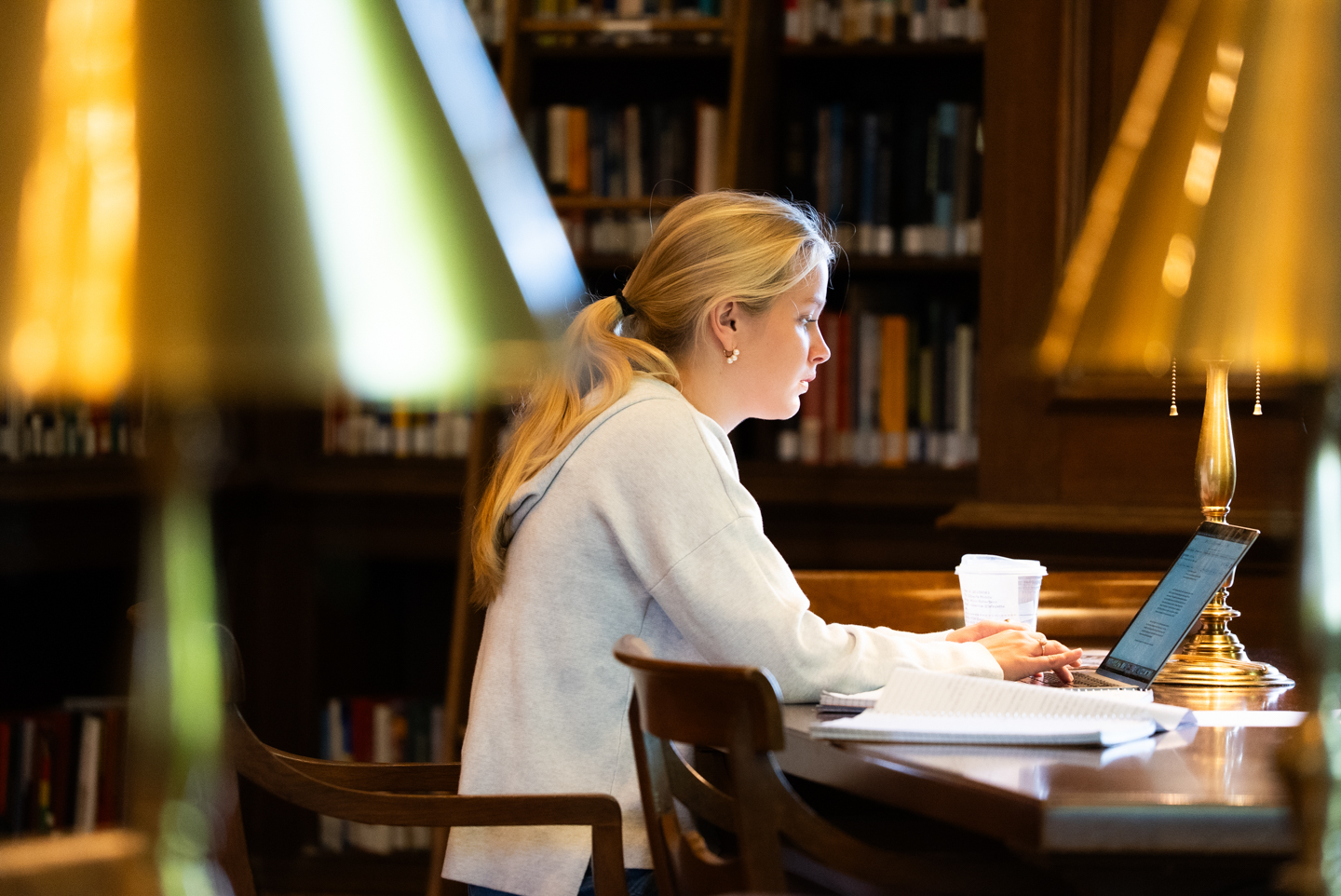 A student studying attentively in Kirby Library with a laptop, surrounded by notebooks and a cup of coffee, preparing for finals week.