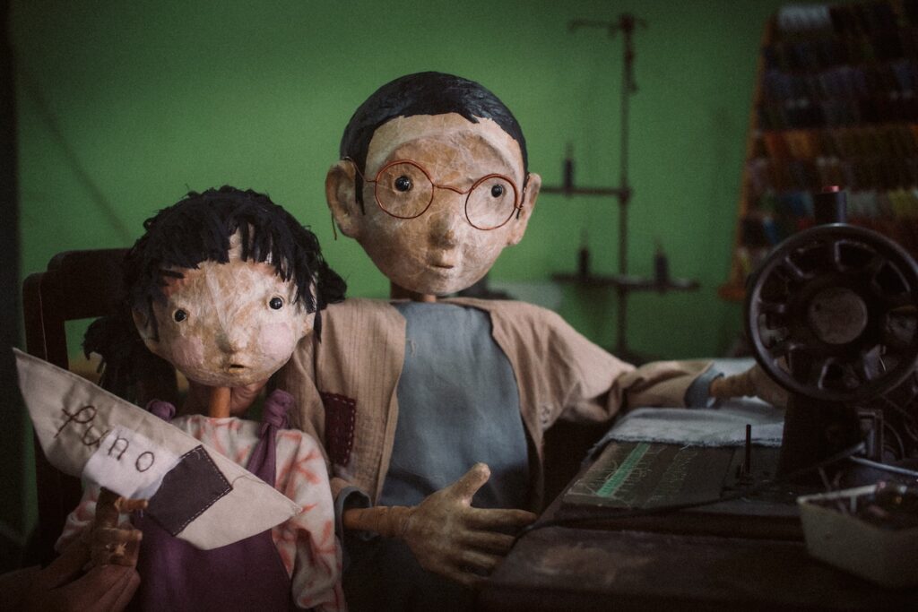 Two puppets from Papermoon Puppet Theatre (contemporary Indonesian puppetry) are shown on a green background.