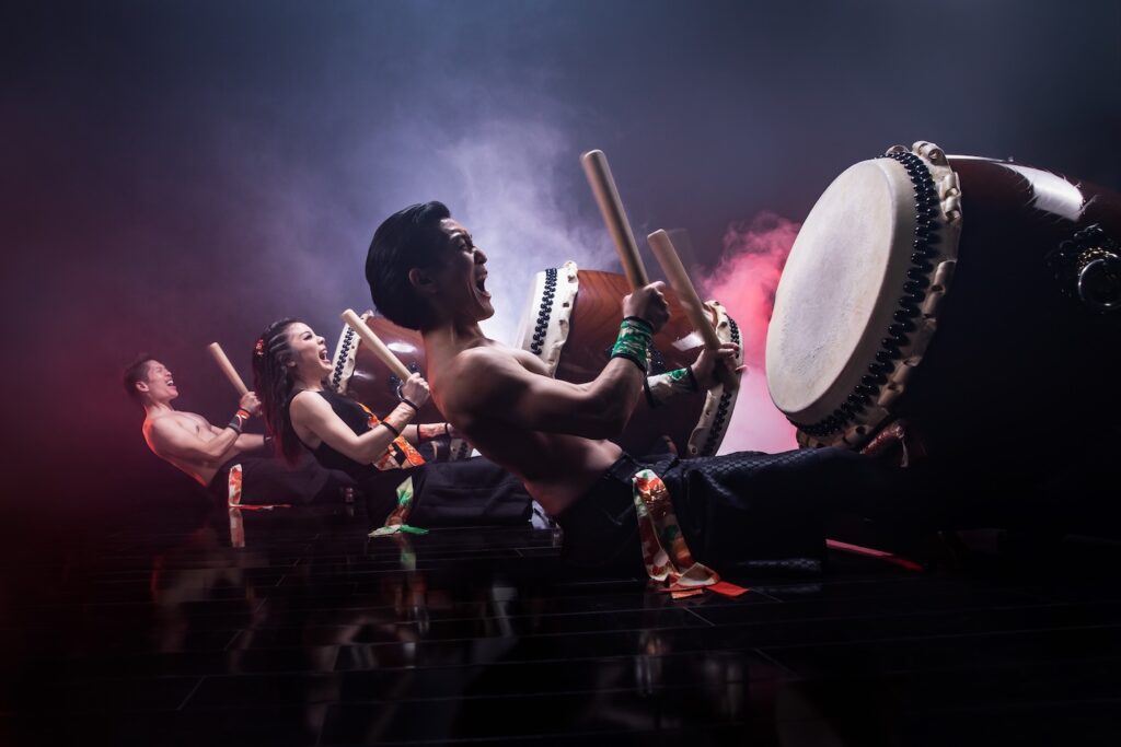 Three drummers are shown in the middle of a performance
