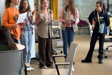 5 Cadette scouts stand in front of a whiteboard in the Dyer Center during a presentation.