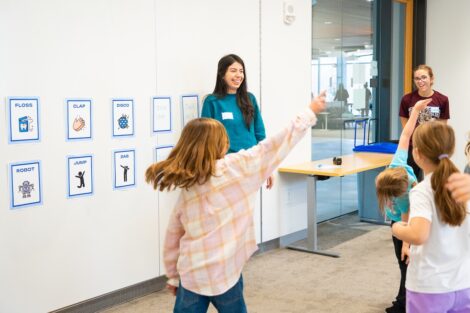 Two Lafayette student volunteers stand in a classroom in RISC as young Girl Scouts dance during Badge Day.