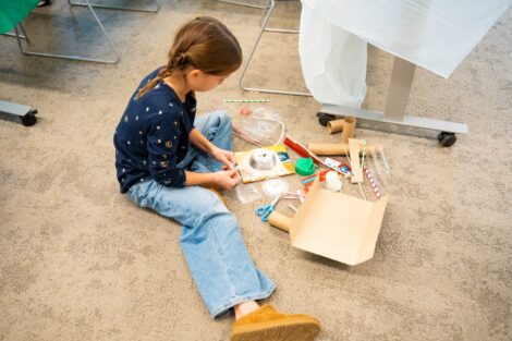 A Girl Scout sits on the floor with recycled materials in front of her, ready to create a Mars rover.
