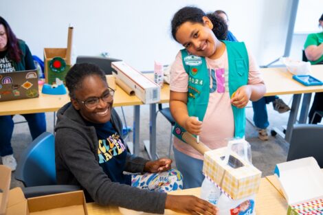 A Girl Scout leader and mom smile as they work together to build a mars rover.