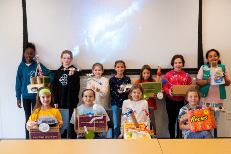 11 Girl Scouts stand in front of a whiteboard showing off their Mars rover creations.