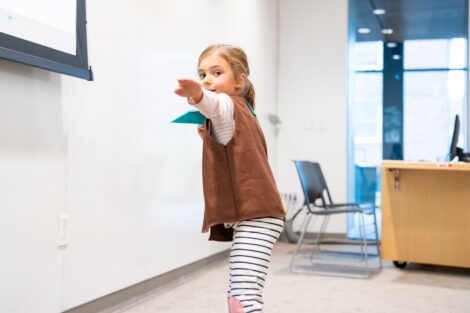 A young Brownie scout is poised to throw a paper airplane.
