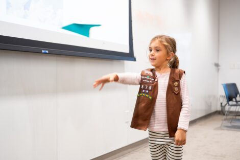 A young Girl Scout in a Brownie vest throws a paper airplane as part of a test to earn her fling flier badge