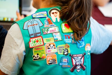 The back of a green Girl Scout vest is covered in patches is shown.