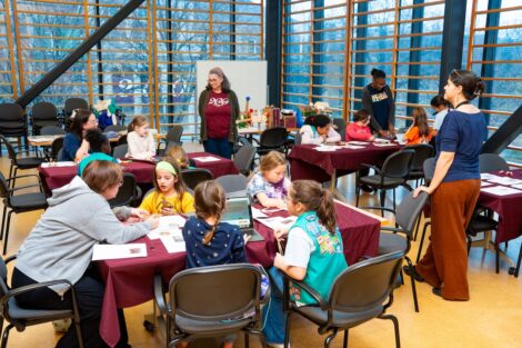 Beth Sica and Ana Ramirez Luhrs work with scouts seated at tables in the Gendebien Room.