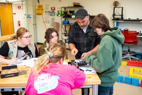 Prof. Alex Brown works with 4 scouts in the robotics lab and is demonstrating how to build the robot.