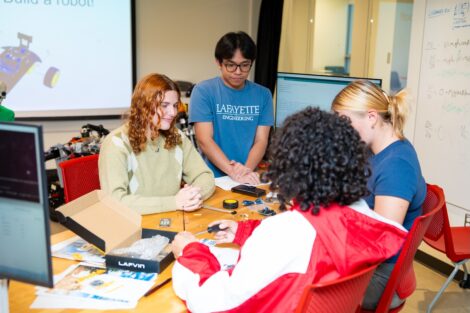 A Lafayette engineering student works with 3 high school scouts in front of a computer as they learn to build and program robots.