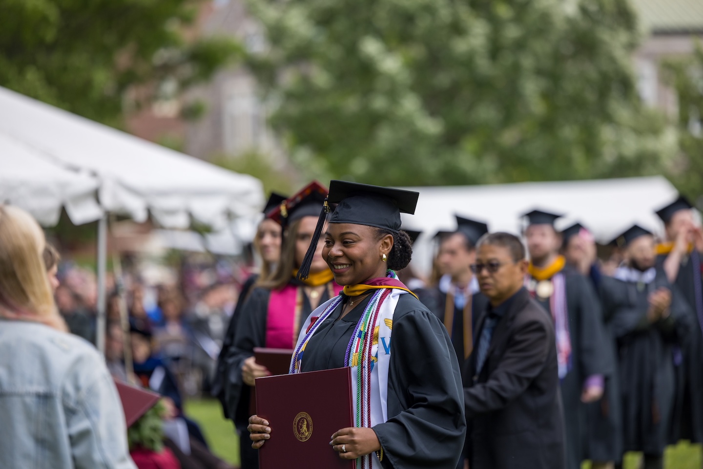 A senior in cap and gown walks forward with diploma in hand as she returns to her seat during the outdoor ceremony.