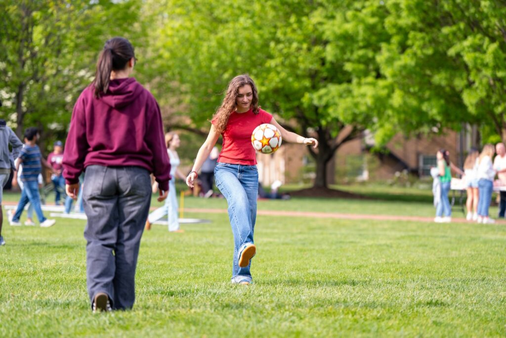A student dribbles a soccer ball across the Quad as another student walks past
