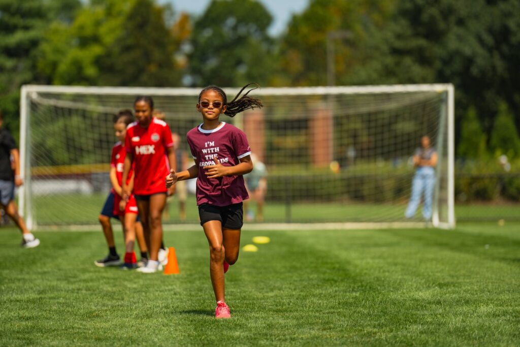 Two girls run across the soccer field at Gummeson Grounds with a goal in the background.